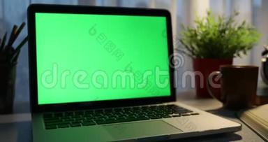 带有绿色屏幕的笔记本电脑。 黑暗的办公室。 多利加入。 完美地放置你自己的图像或视频。 正在使用的技术绿色屏幕。 语文